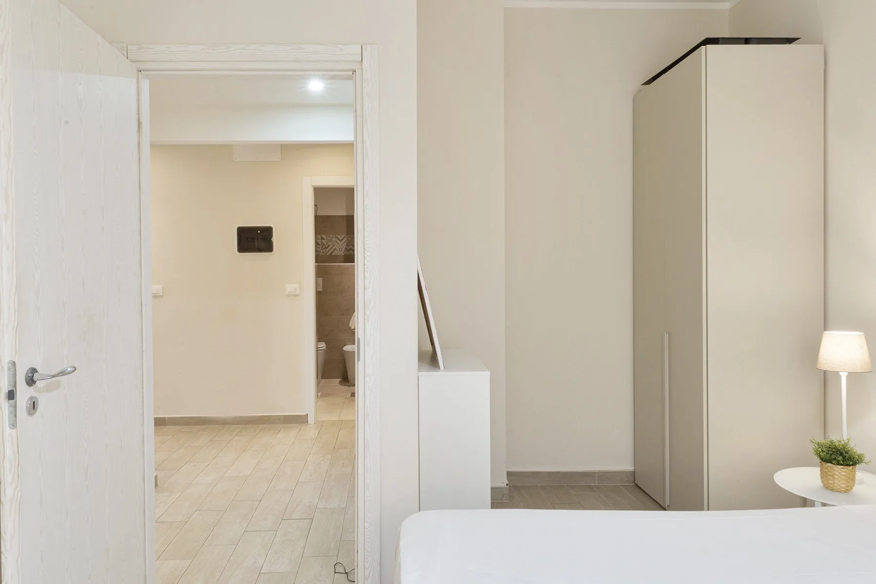 A bedroom with a bed, a tall wardrobe, and an open doorway.