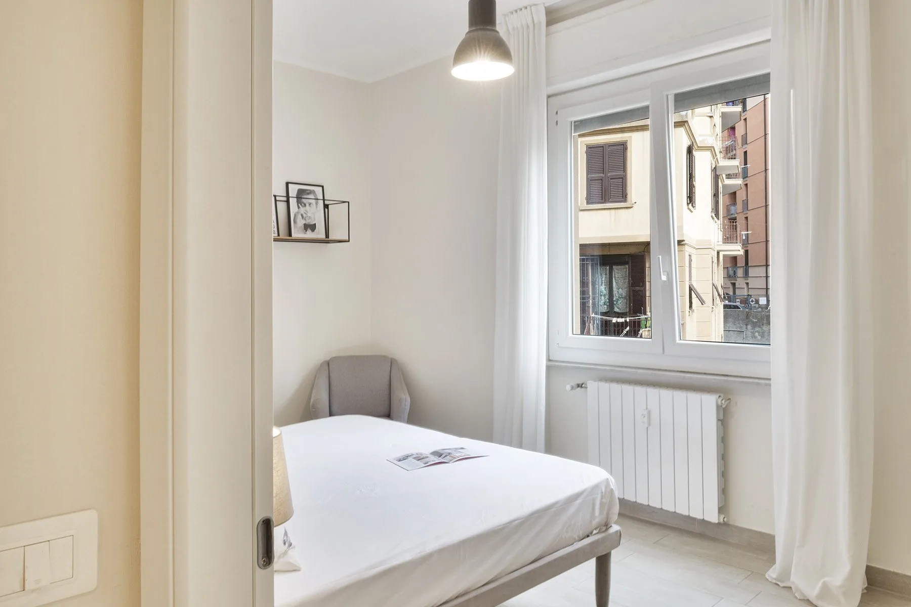 A bright bedroom with a neatly made bed beside a large window.