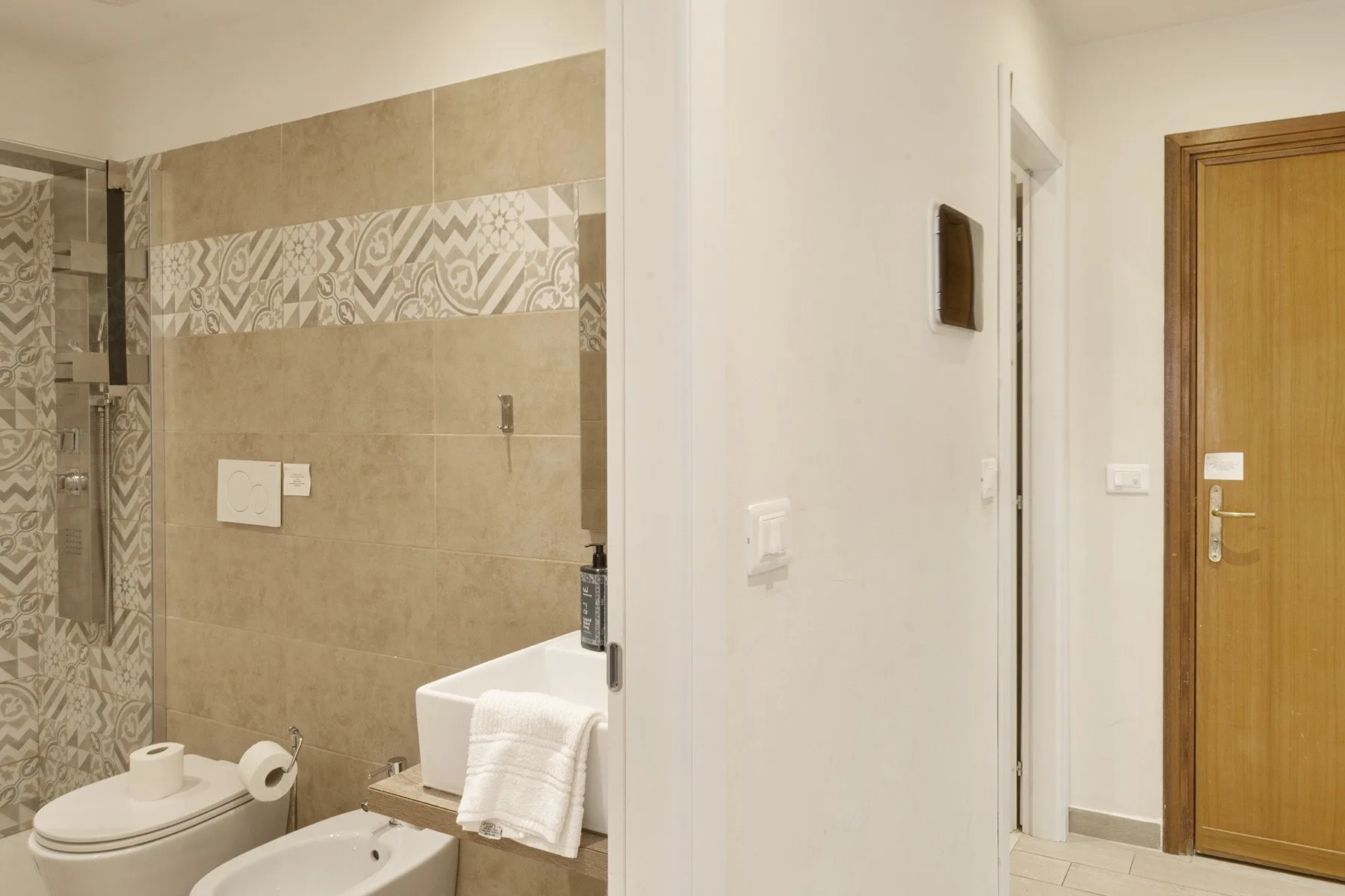 A bathroom with a patterned tile wall and a towel draped over the sink.
