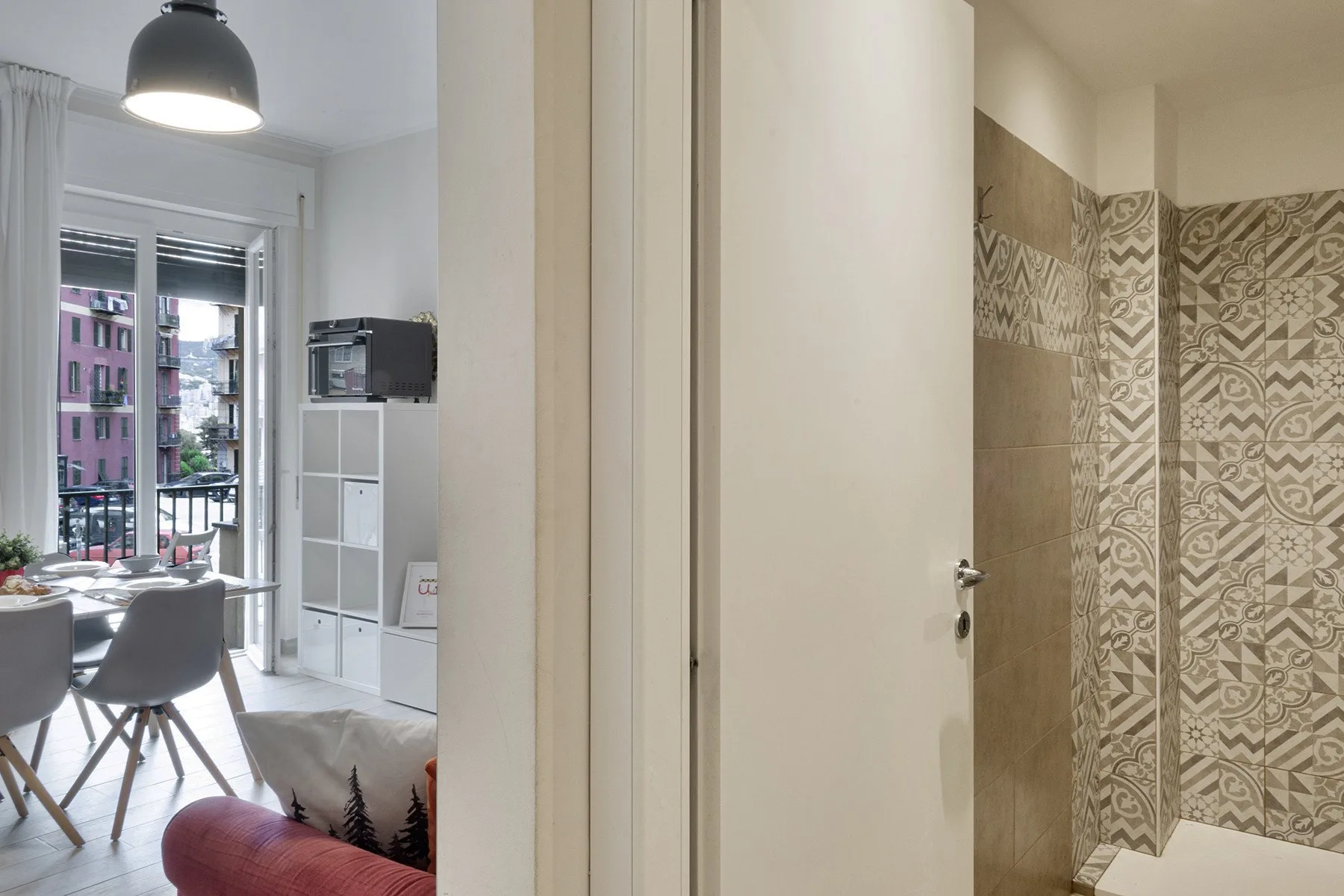 A bathroom with patterned wall tiles beside an open doorway to a dining area.