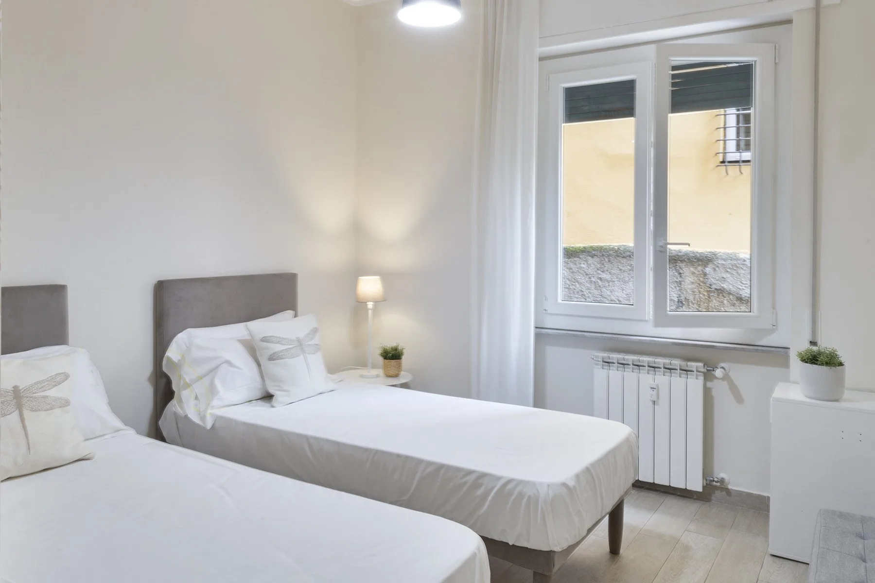 A bright bedroom with two single beds and a large window.