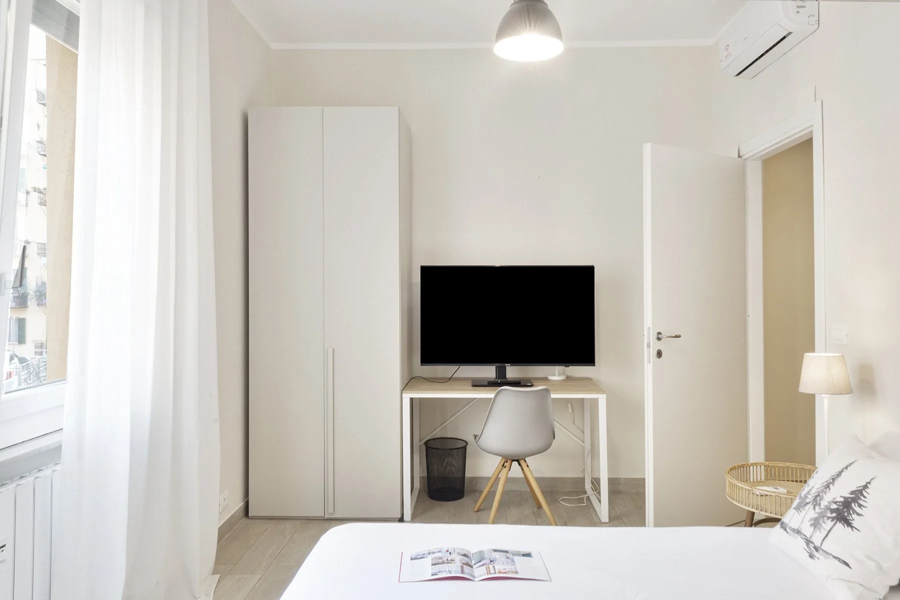 A bright bedroom with a television on a desk beside a tall wardrobe.