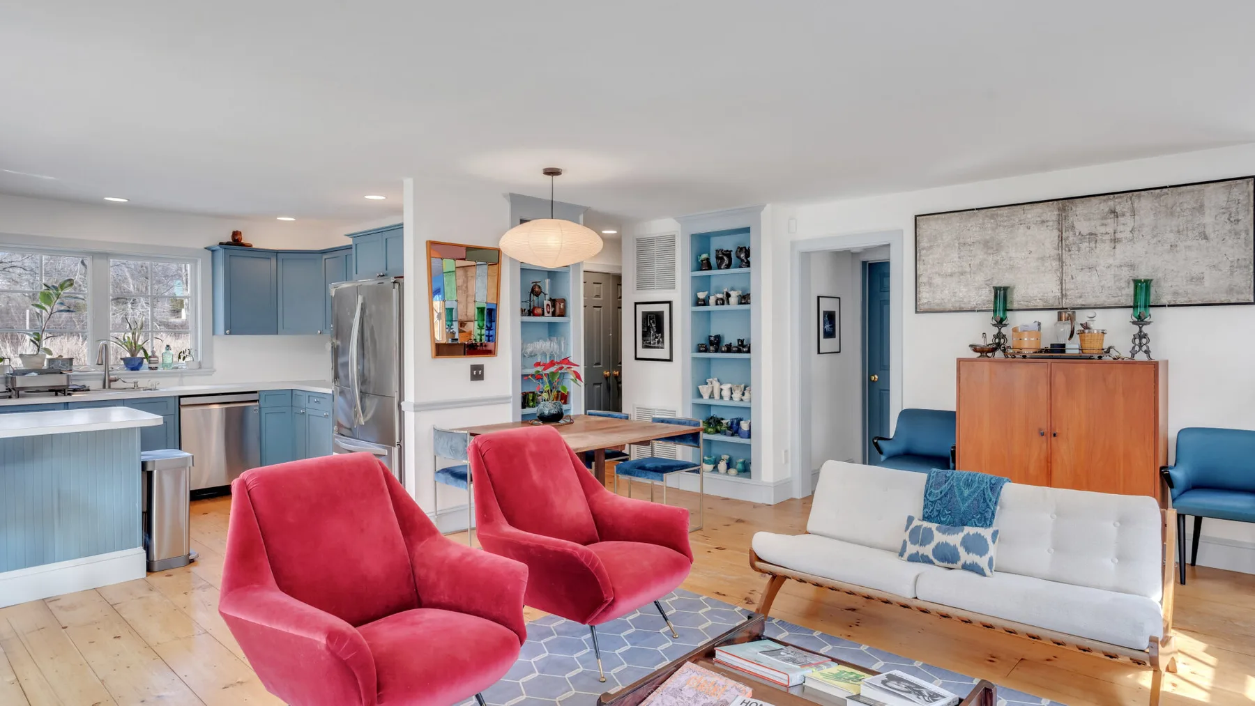 Una sala luminosa con asientos rojos, un sofá blanco y una cocina azul.