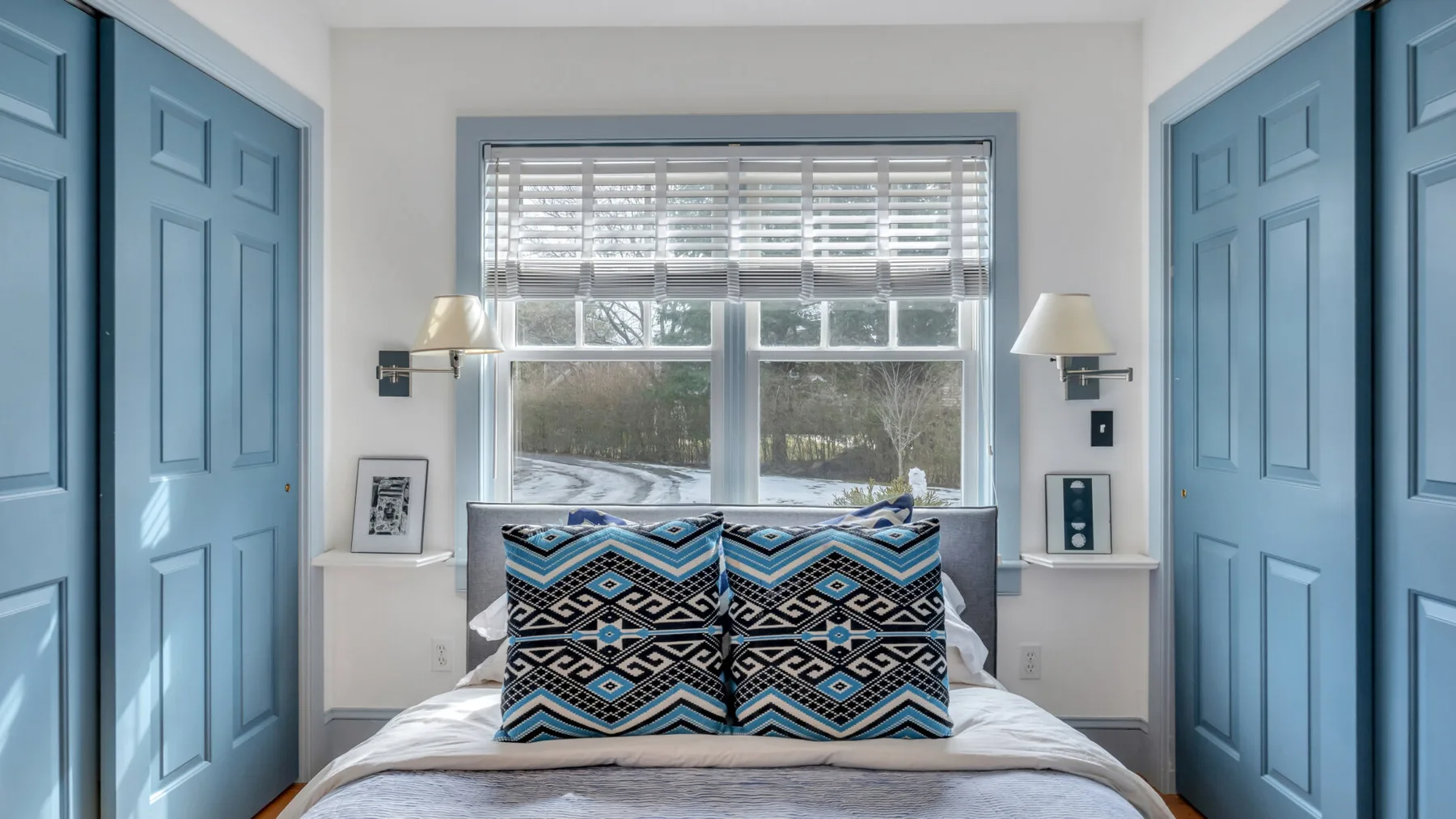 Un dormitorio con una cama y cojines estampados entre puertas azules con paneles.
