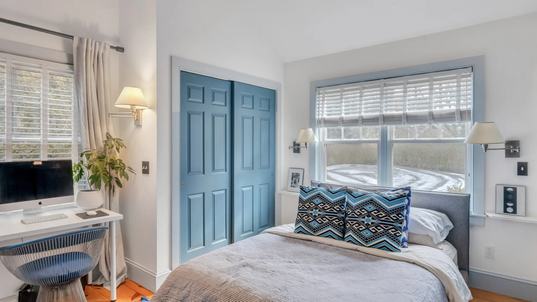 Un dormitorio con una cama, puertas dobles azules y ventanas con persianas.