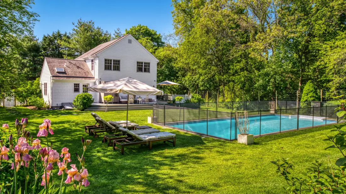 Una piscina en el patio está junto a una casa blanca y asientos de jardín.
