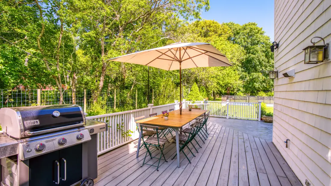 Una terraza exterior con una mesa de comedor, una sombrilla y una parrilla.