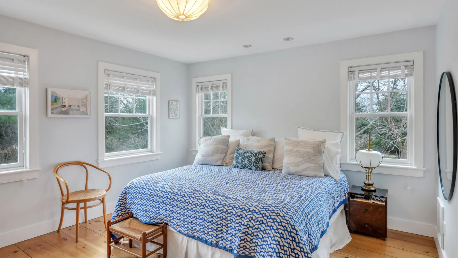Un dormitorio luminoso con una cama cubierta por una colcha azul estampada y varias ventanas.