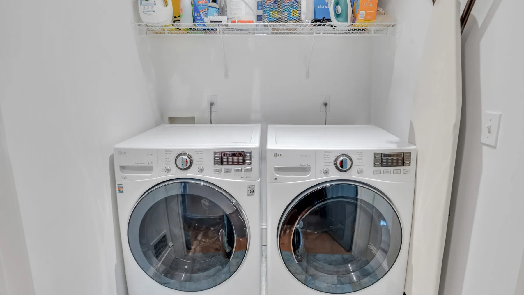 Zona de lavandería con dos máquinas de carga frontal bajo un estante con productos de limpieza.