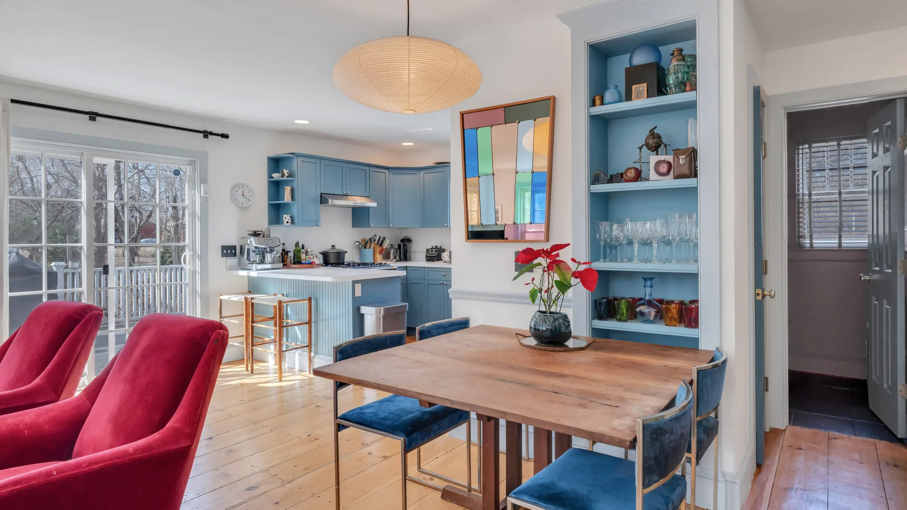 Un comedor luminoso con una mesa de madera, armarios azules y asientos rojos.