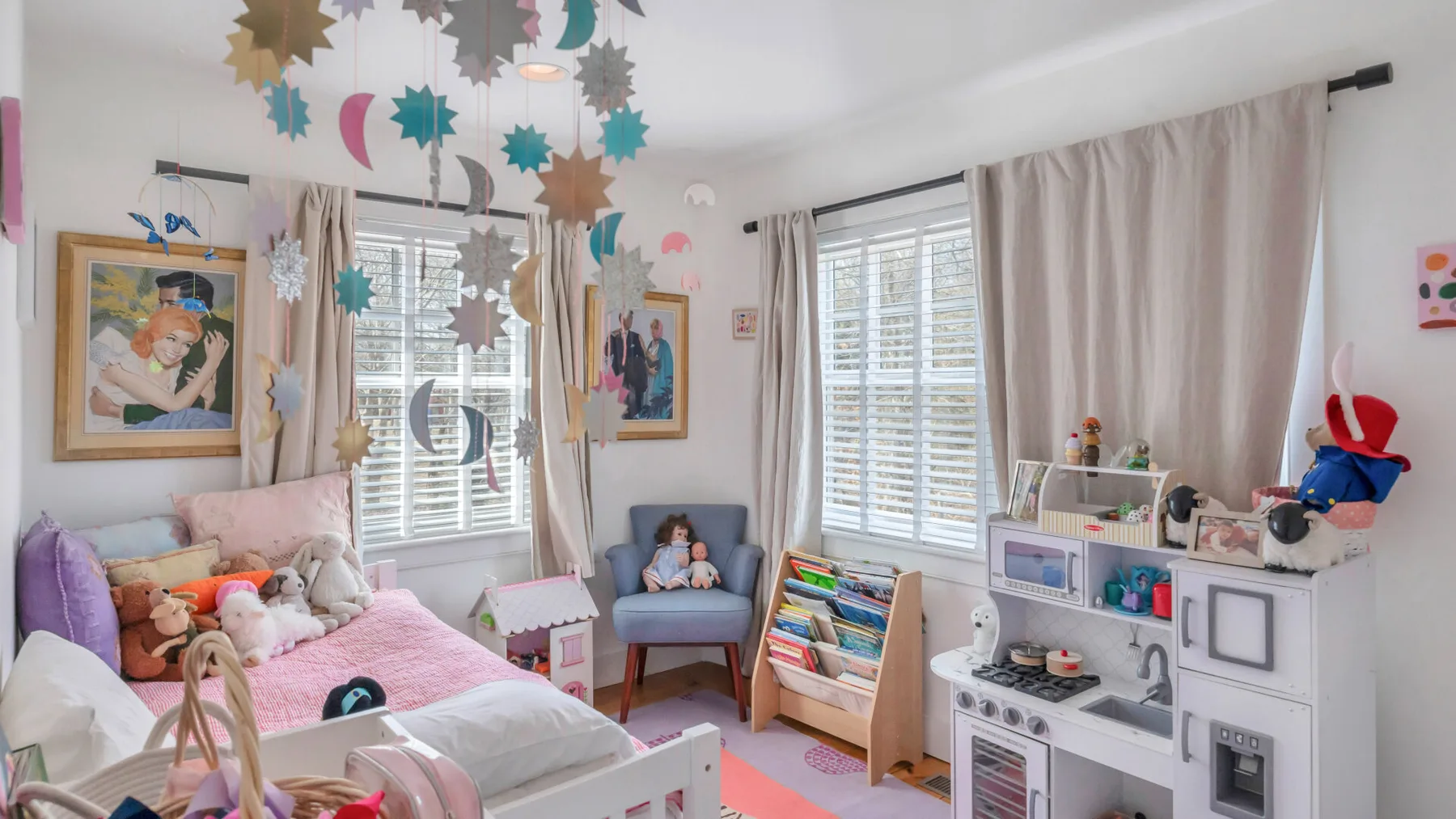 Un dormitorio infantil colorido tiene una cama rosa, ventanas y espacio para juguetes.