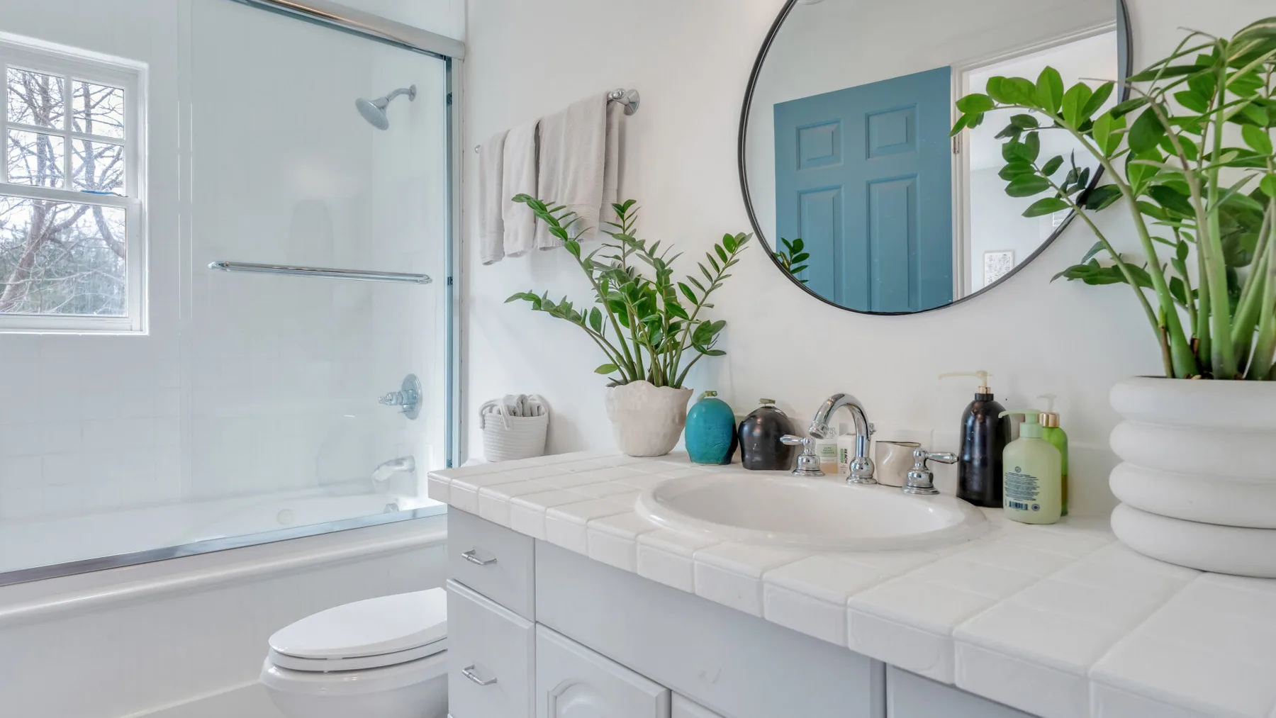Un baño luminoso con bañera, lavabo y plantas.