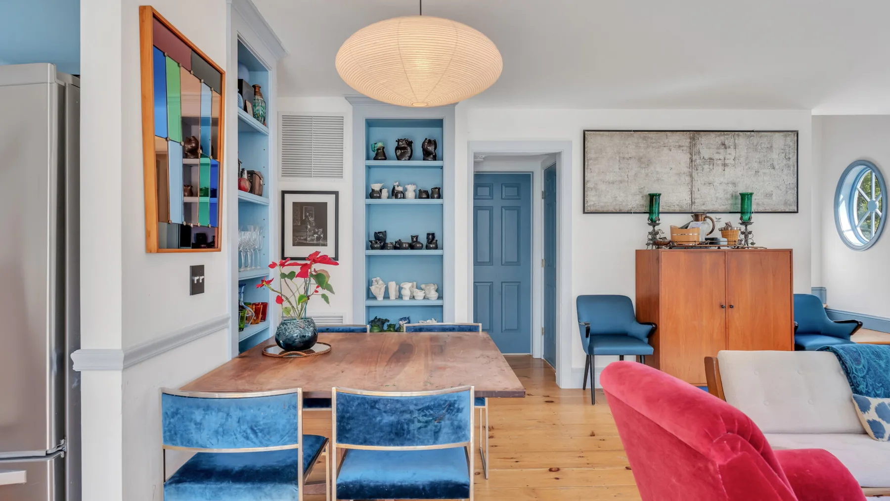 Un salón-comedor luminoso con asientos azules, una mesa de madera y estantes empotrados.