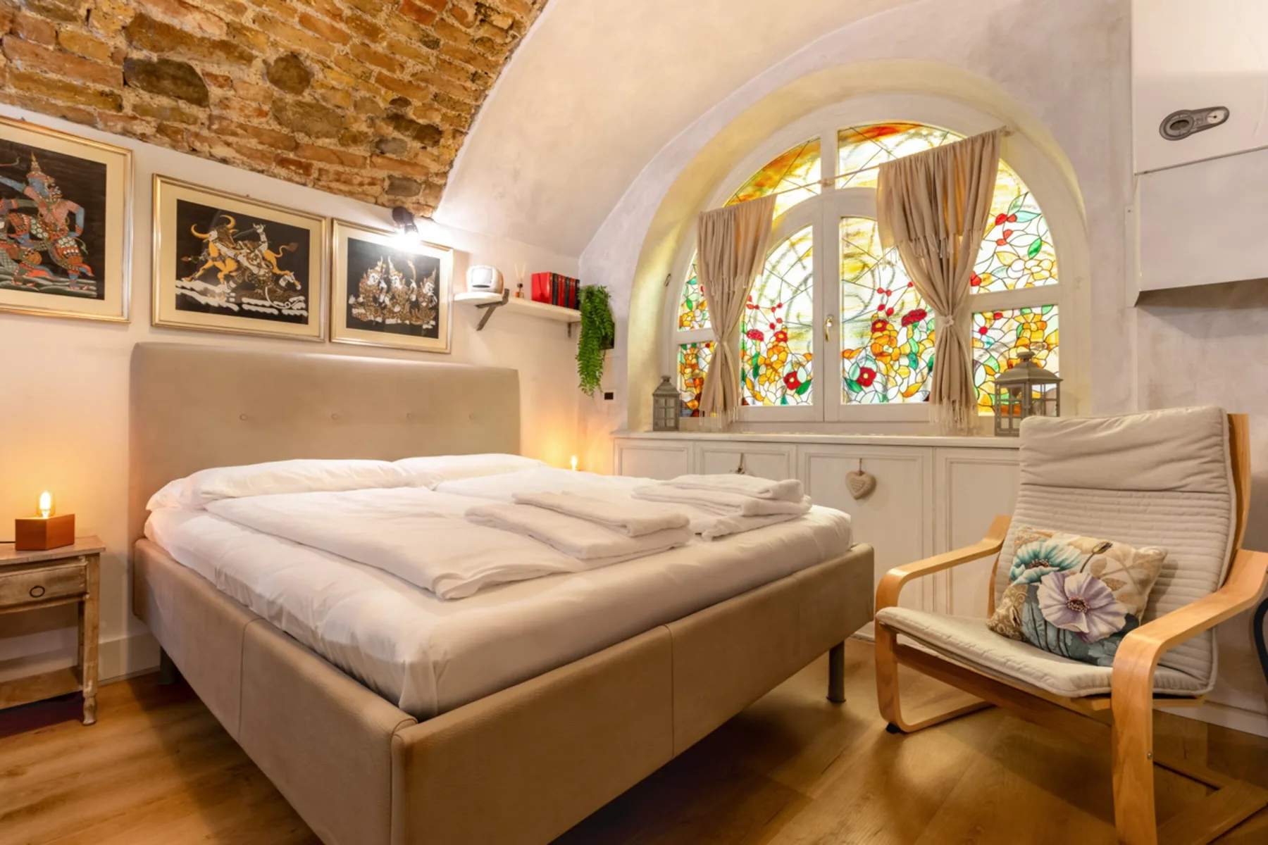 Un dormitorio con una cama grande, una silla de madera y coloridas ventanas de vidrieras.
