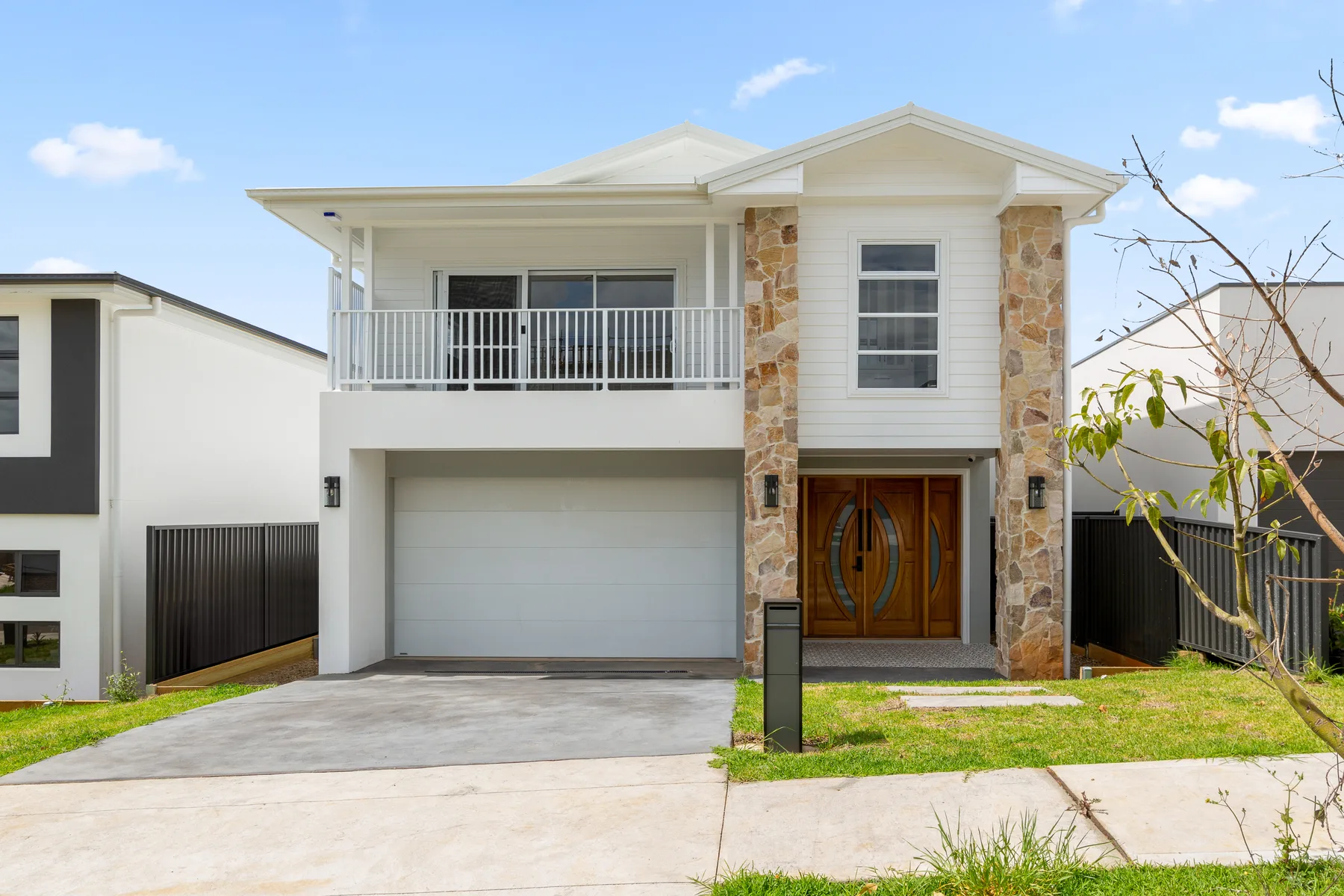 A two-storey house has a balcony, stone accents, and a wide driveway.