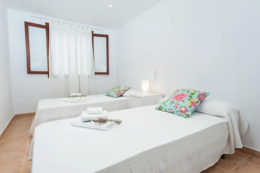 A bright bedroom with two beds and colorful floral pillows.