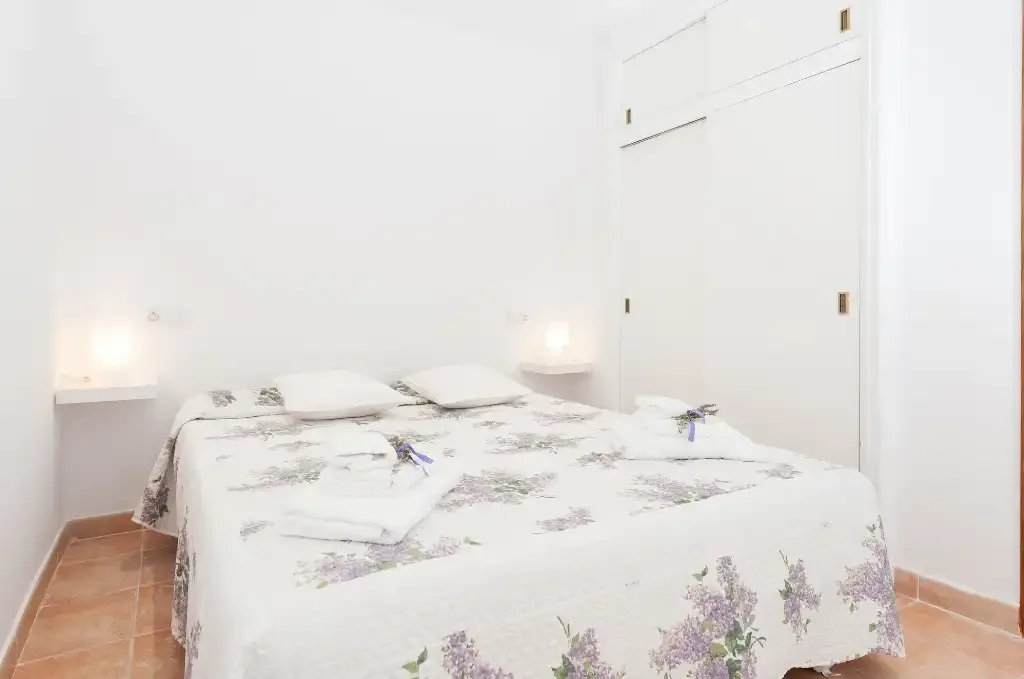 A bright bedroom with floral bedding and small bedside lights.