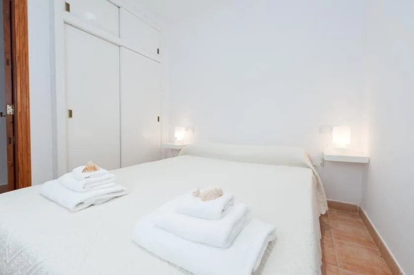 A bright bedroom with white bedding and folded towels on the bed.