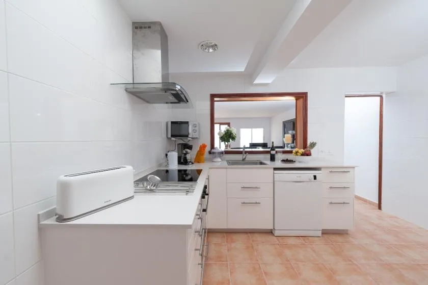 A bright kitchen with white counters and cabinets, viewed toward a sink and window.