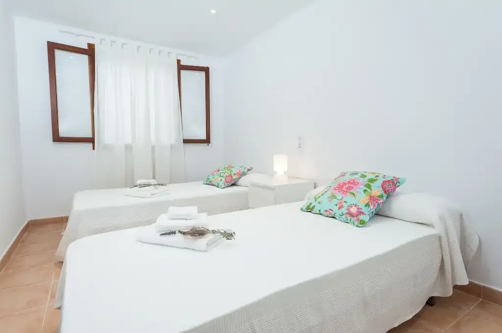 A bright bedroom with two beds and floral pillows.