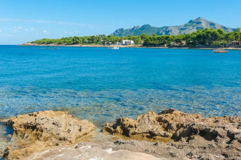 Coastal seascape with clear blue water, rocky shore, and a distant tree-lined coast.