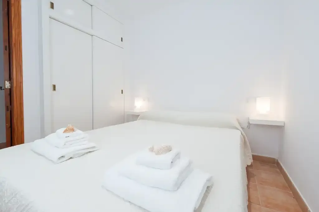 A bright bedroom with a neatly made bed and folded towels.