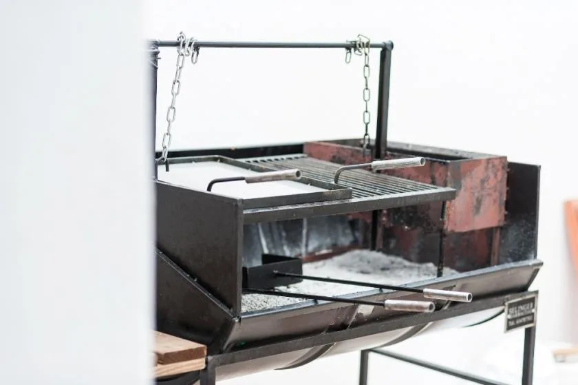 A large barbecue grill with metal grates and an adjustable hanging rack.