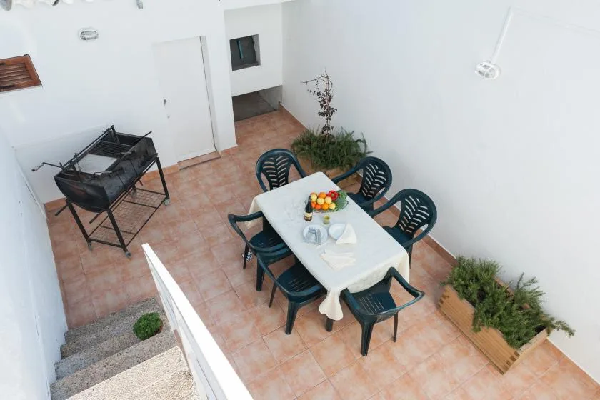 A tiled patio has a dining table with chairs and a small grill.