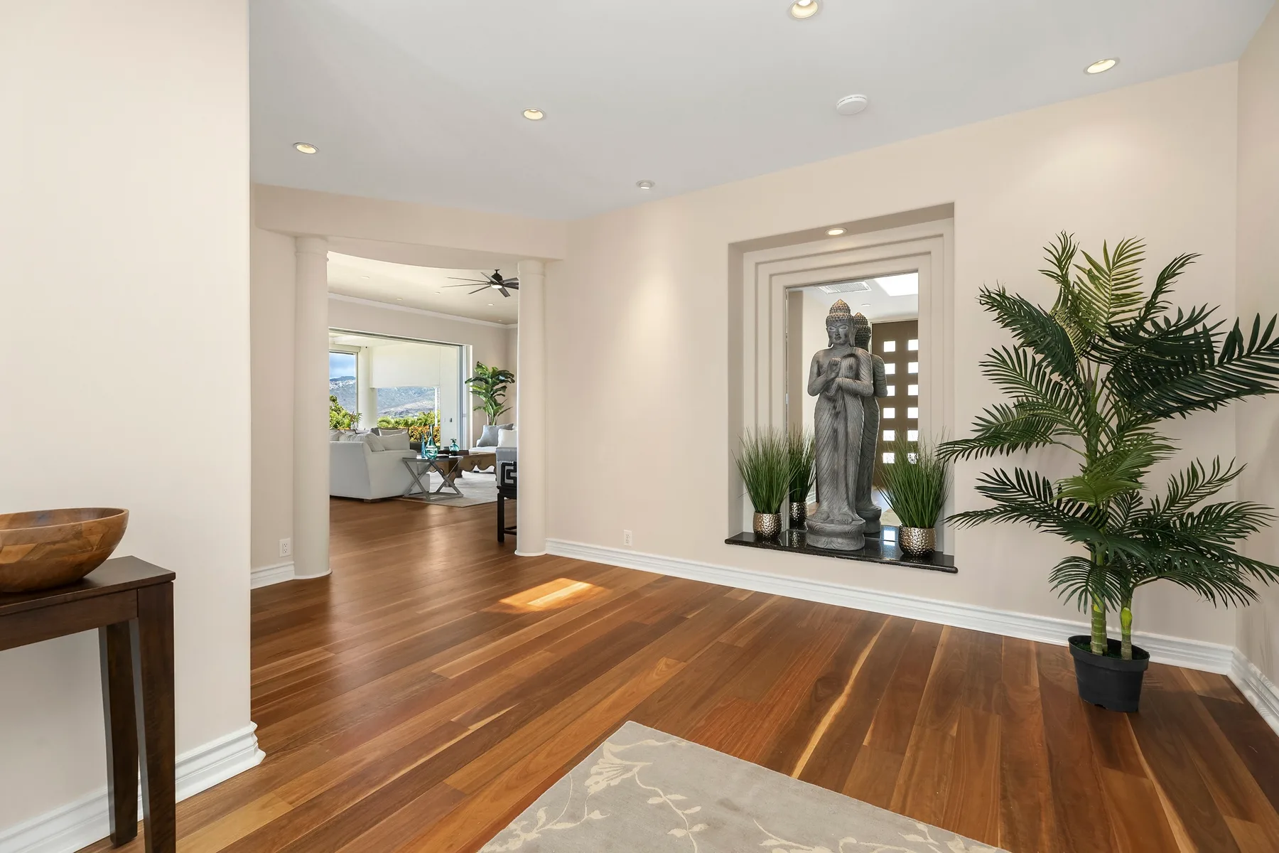 Un pasillo interior luminoso con suelo de madera, plantas en macetas y una estatua.