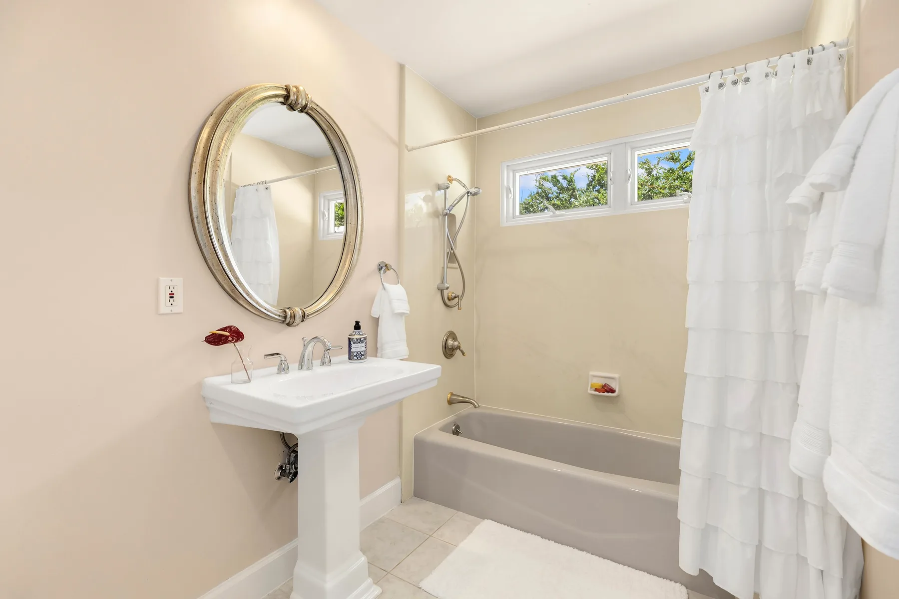 Un baño con lavabo de pedestal, espejo ovalado y bañera detrás de una cortina de ducha.