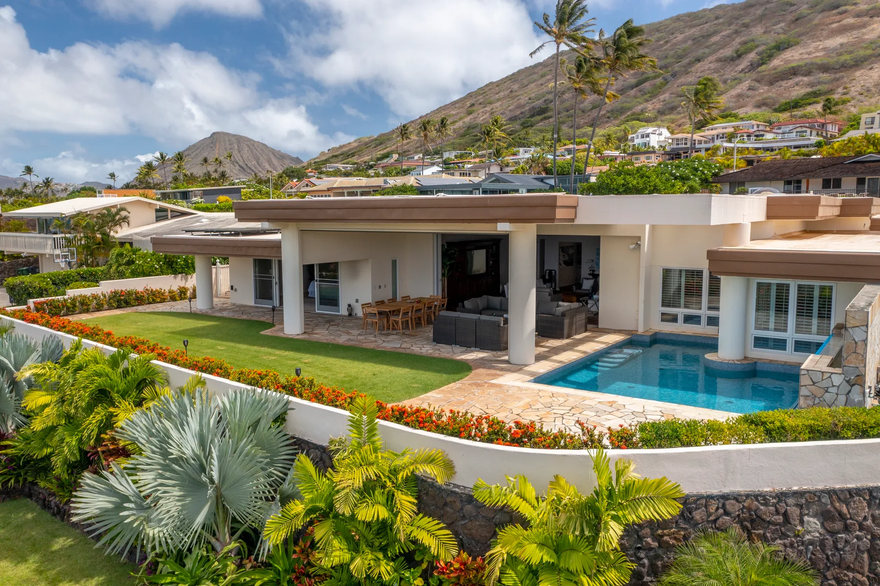 Una casa moderna con piscina, jardín y una ladera al fondo.