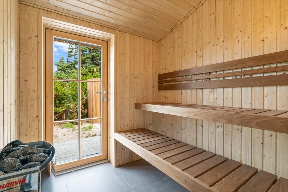 Una sauna revestida de madera con bancos escalonados y una puerta de vidrio hacia la vegetación.