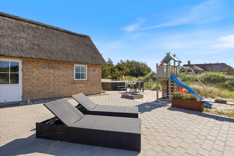 Un patio exterior pavimentado con asientos reclinables y una estructura de juego infantil.