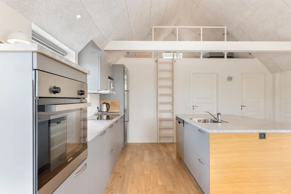Una cocina luminosa con horno, isla central y suelo de madera.
