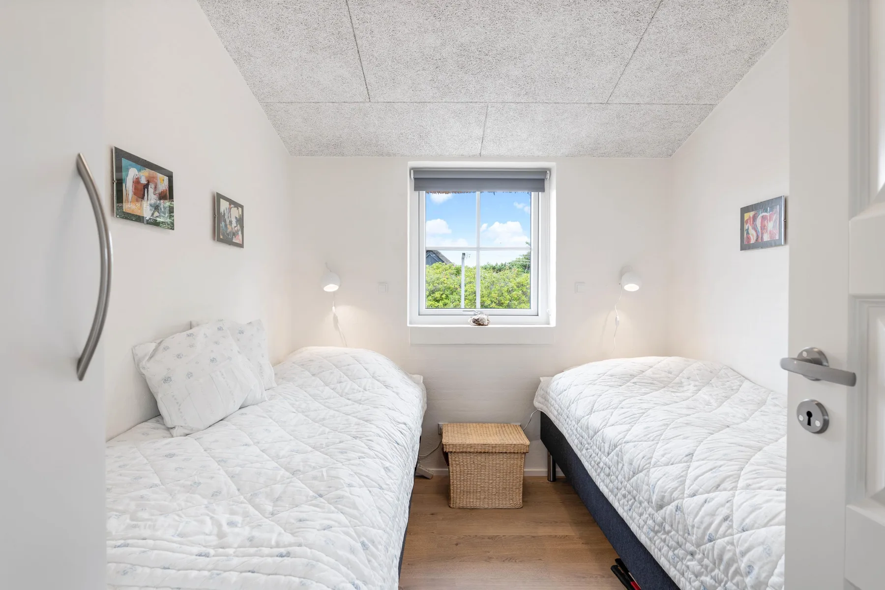 Un dormitorio luminoso con dos camas individuales y una ventana con vistas a zonas verdes.