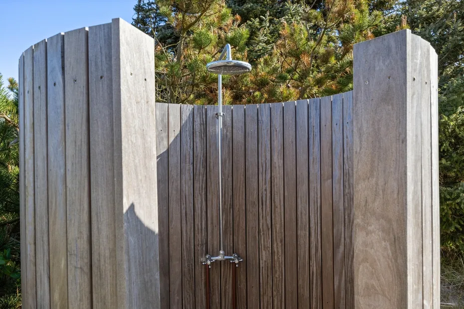 Una ducha exterior está frente a una pantalla de madera entre árboles.