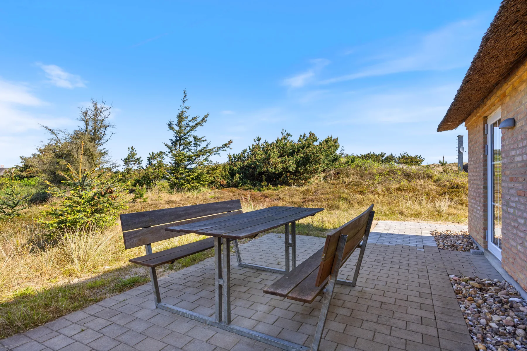 Un patio exterior con mesa y asientos da a un paisaje cubierto de hierba.