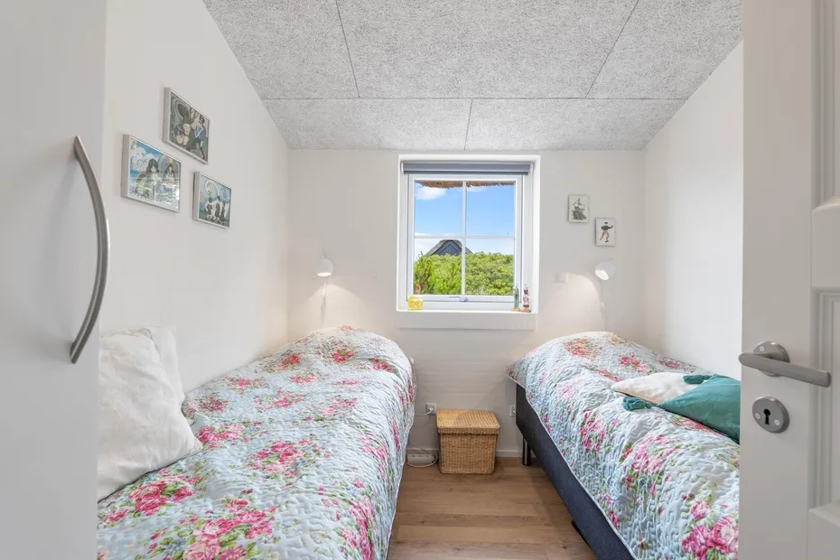 Un dormitorio con dos camas, ropa de cama floral, una ventana y una mesita.
