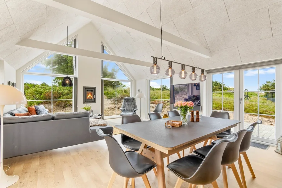 Un luminoso espacio diáfano de sala y comedor con grandes ventanas y una mesa de madera.