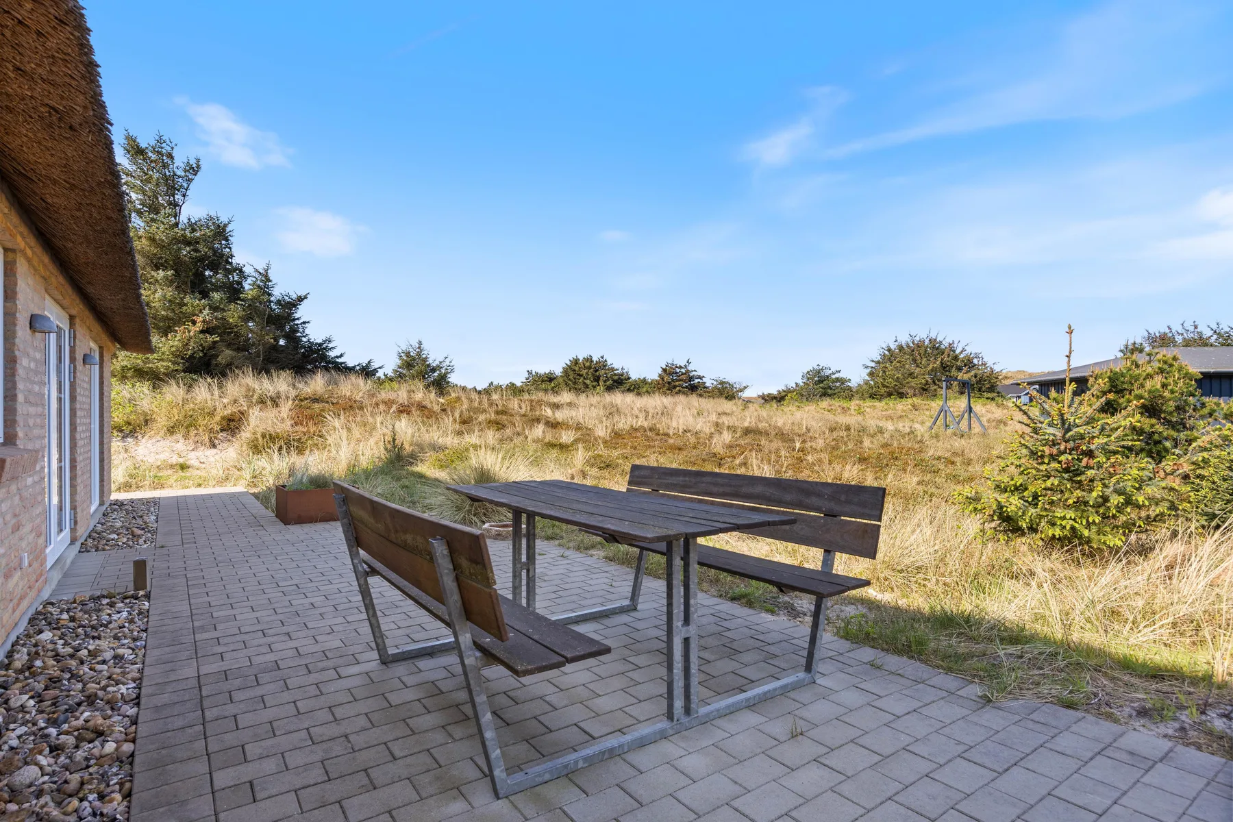Un patio exterior con una mesa y bancos junto a una casa.