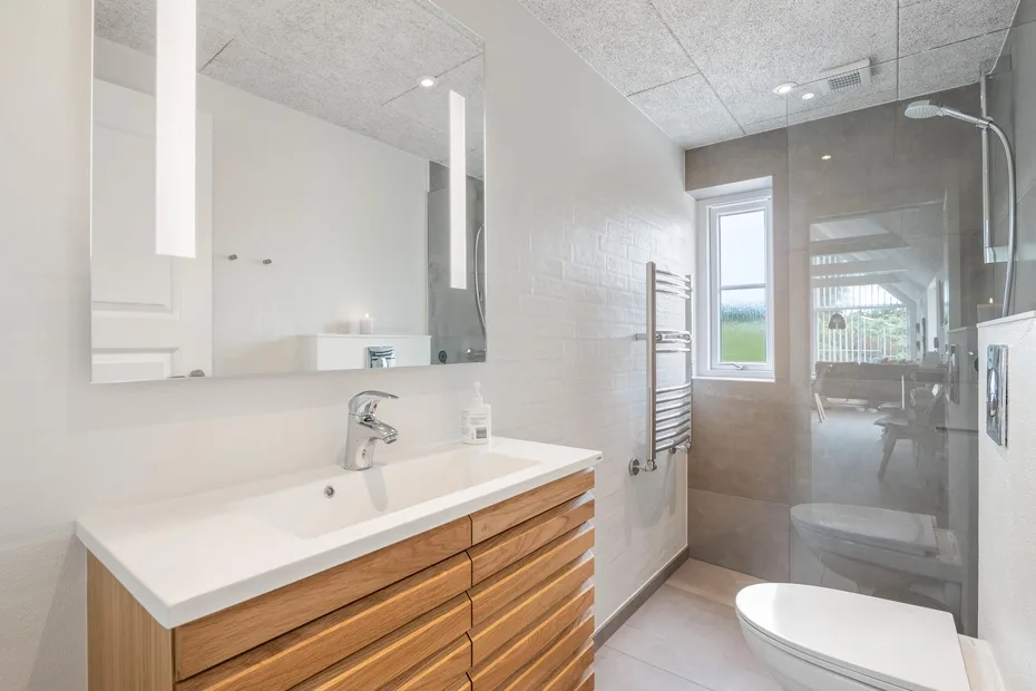 Un baño luminoso con lavabo de frente de madera, espejo y ducha de vidrio.