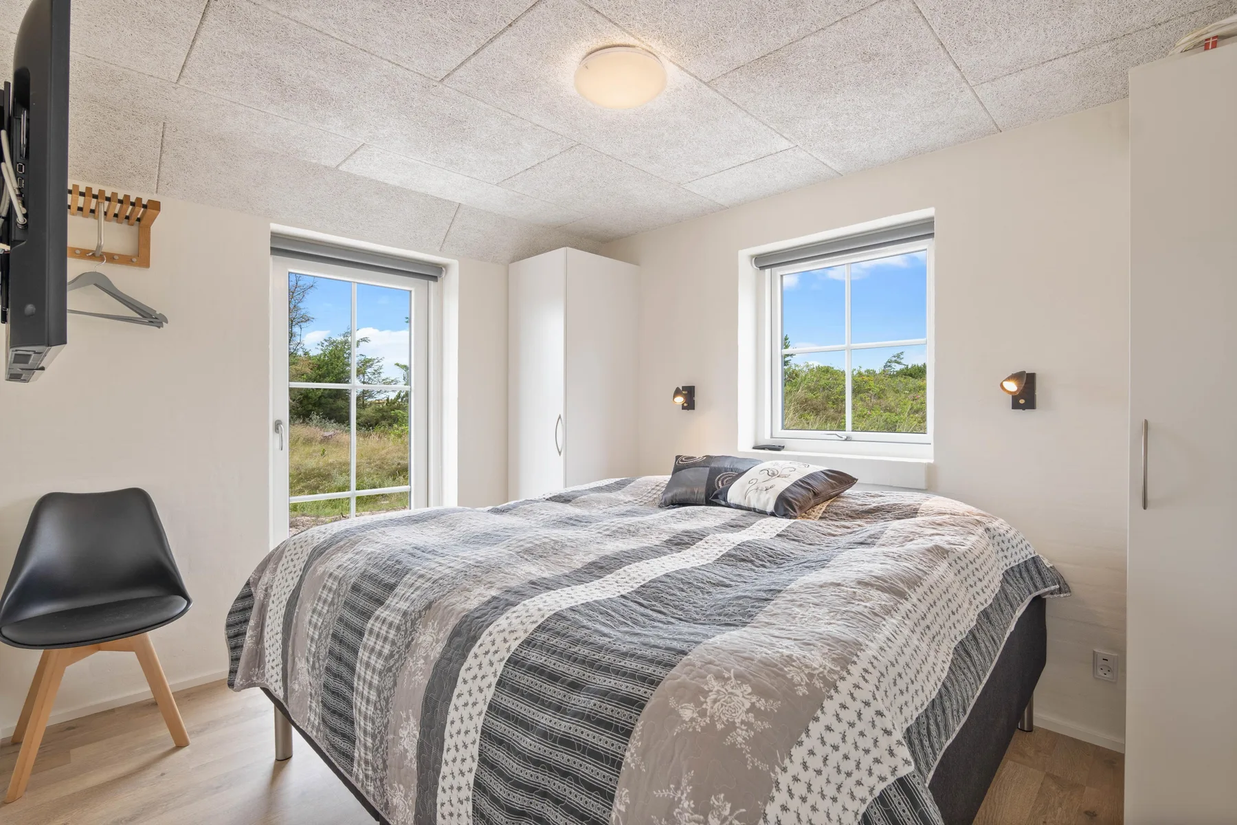 Un dormitorio con una cama grande, ropa de cama estampada y dos ventanas.