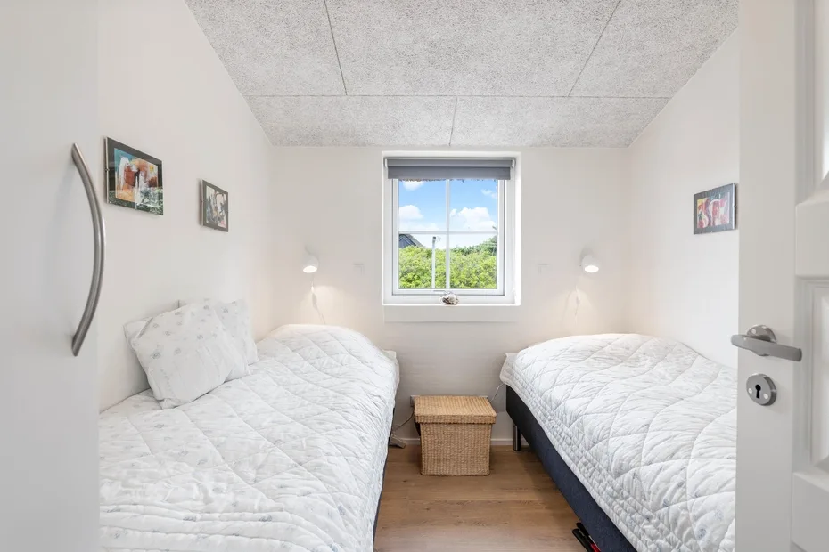Un dormitorio luminoso con dos camas individuales y una ventana con vistas a la vegetación.