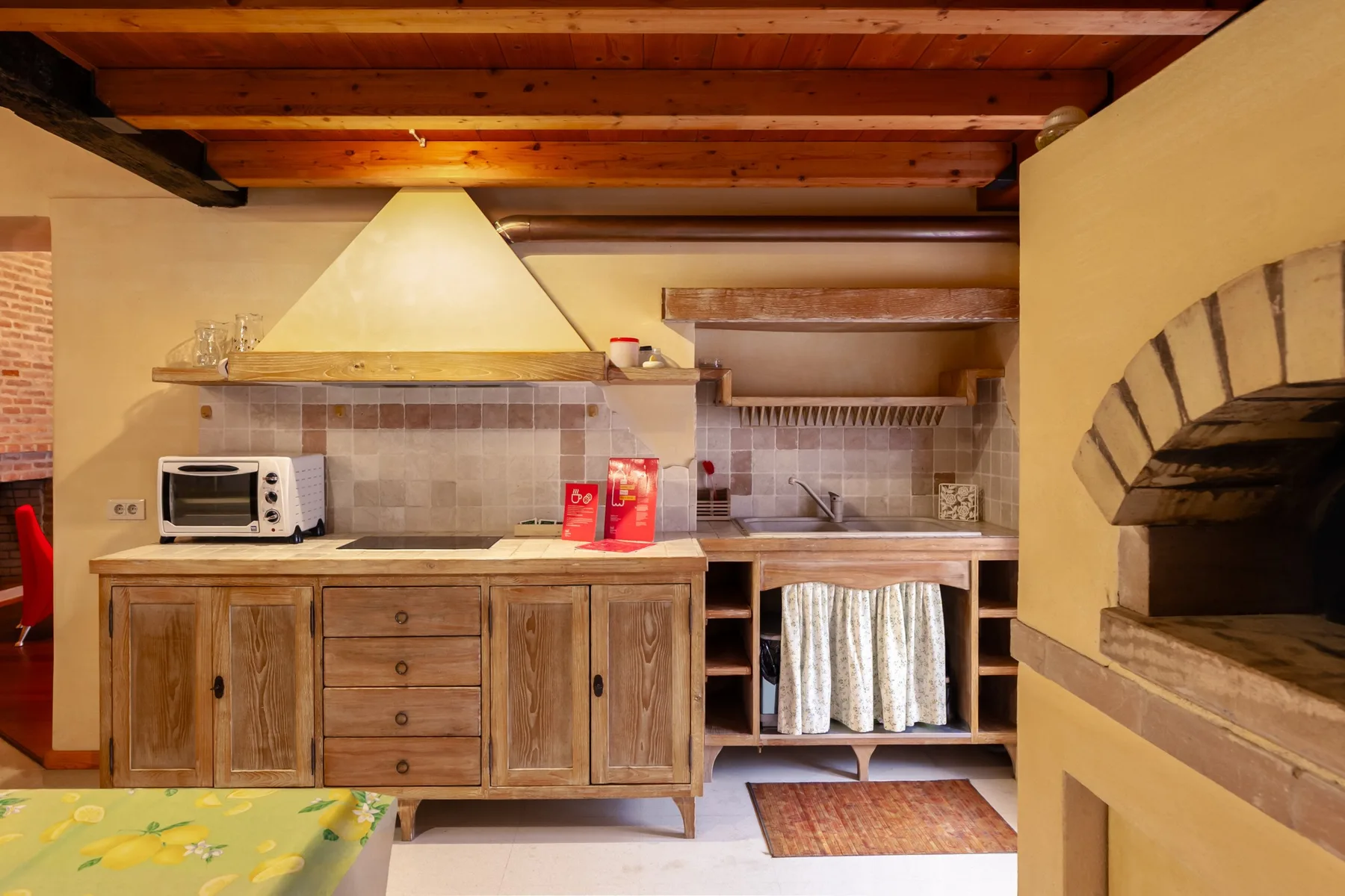 A rustic kitchen with wooden cabinetry, a countertop, and an open hearth.