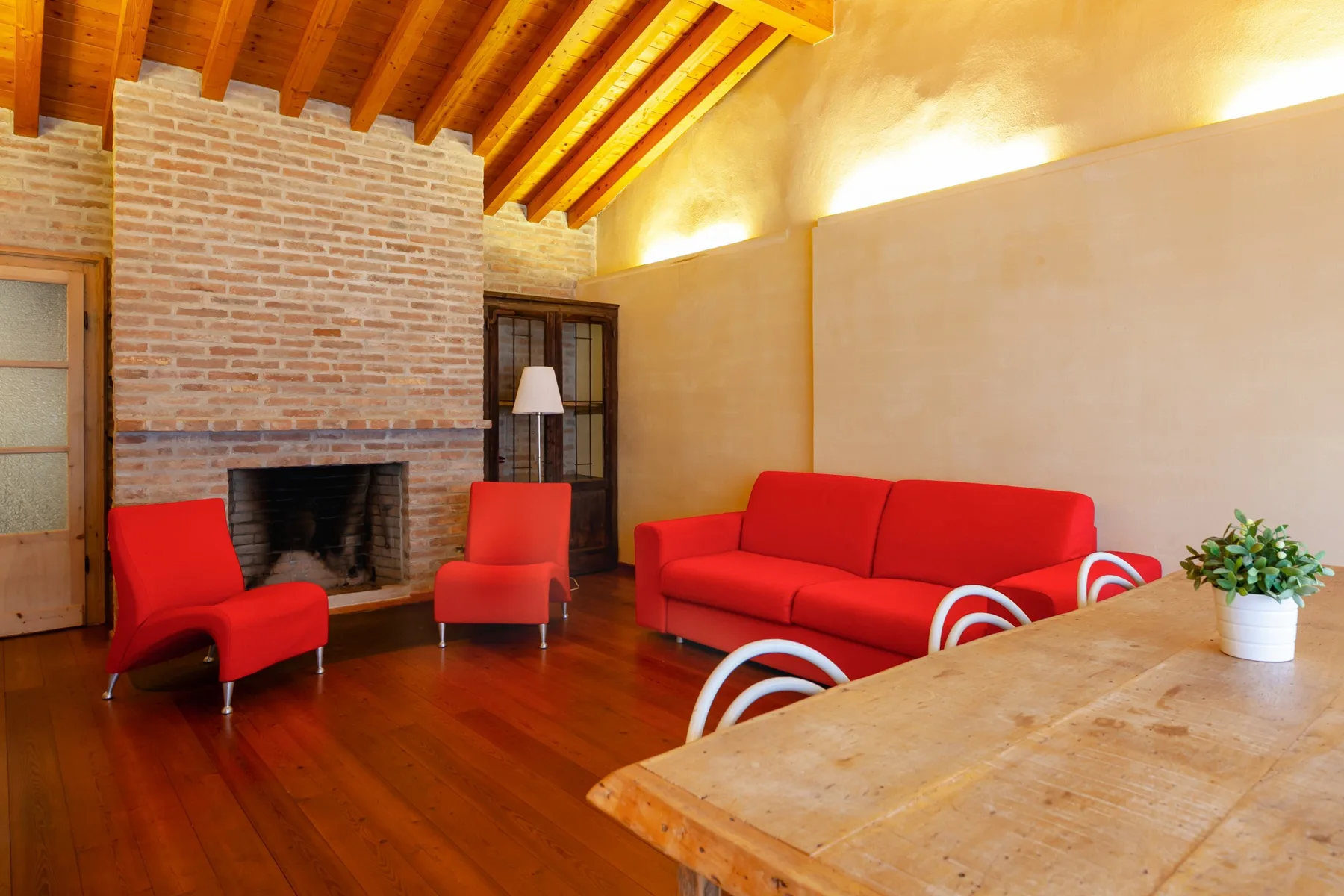 A living room with red seating, a brick fireplace, and exposed wooden ceiling beams.