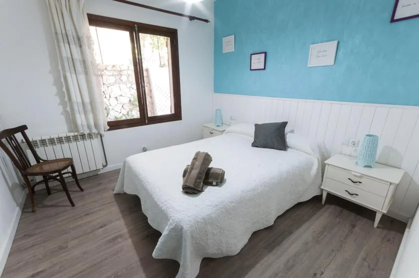 A bedroom with a white bed, turquoise wall, and window.