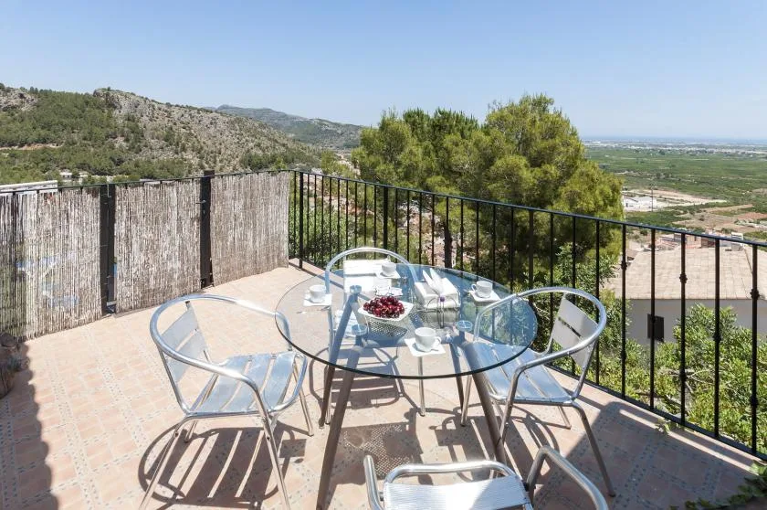 A tiled outdoor terrace has a glass dining table and views of the surrounding hills.