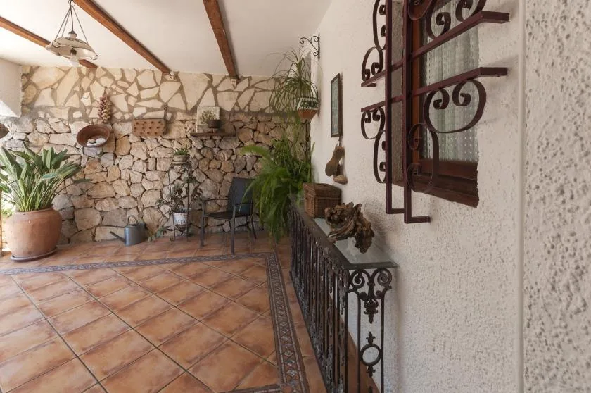 A rustic patio with tiled flooring, stone walls, and potted plants.