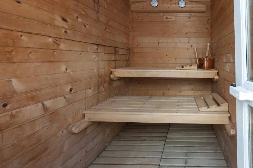 A wood-paneled sauna room with tiered wooden benches and a bucket.
