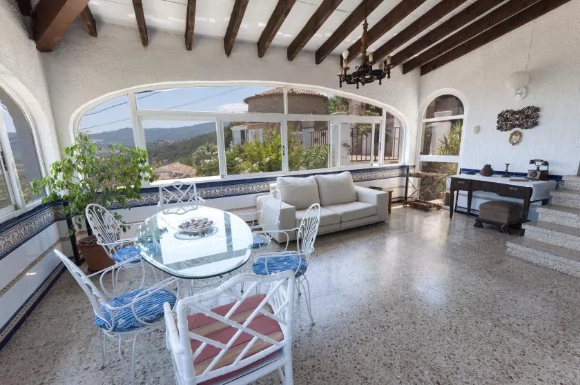 A bright living and dining area has large arched windows and a table with chairs.